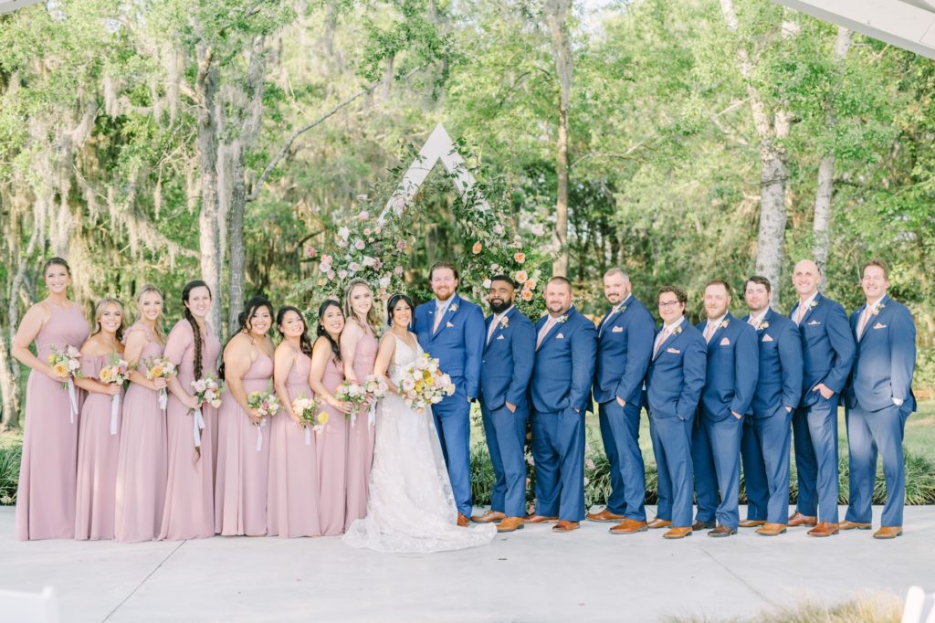 Groomsmen in blue and bridesmaids in pink stand in front of rose alter by Christina Elliott Photography. pro wed photographer Houston #ChristinaElliottPhotography #ChristinaElliottWeddings #Houstonwedding #TheSpringsVenue #EastHoustonweddings #sayIdo