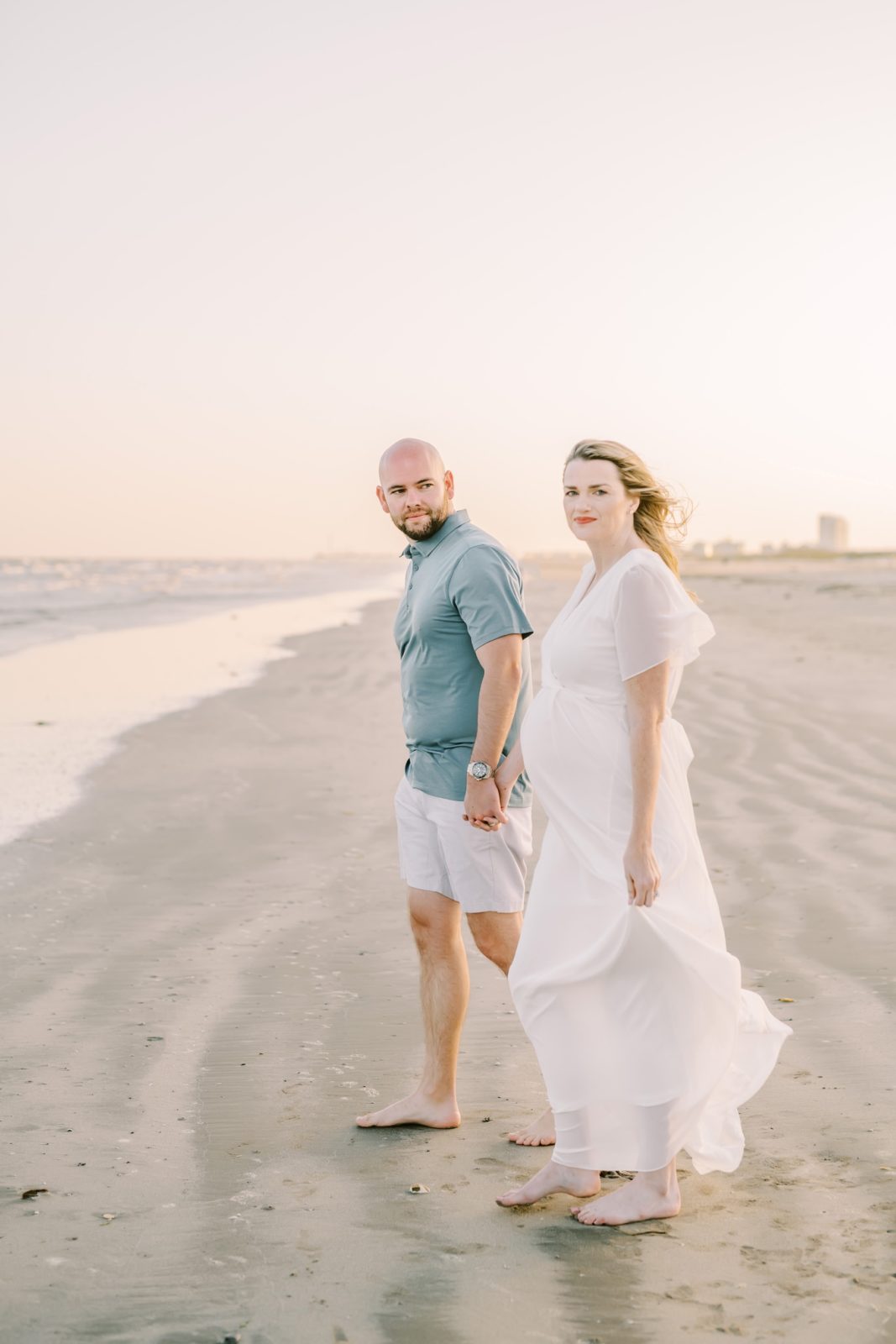 With hair blowing in the wind a pregnant woman smiles on the beach by Christina Elliott Photography. Husband and wife #ChristinaElliottPhotography #ChristinaElliottFamilies #GalvestonPhotography #Beachmaternityphotography #Texasfamilyphotographers