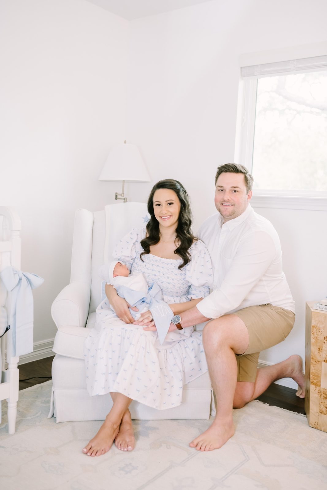 In a nursery in Houston newborn parents smile for a family portrait with their baby by Christina Elliott Photography. family of three #ChristinaElliottPhotography #ChristinaElliottNewborns #HoustonLifestyleNewborns #HoustonFamilyPhotographer