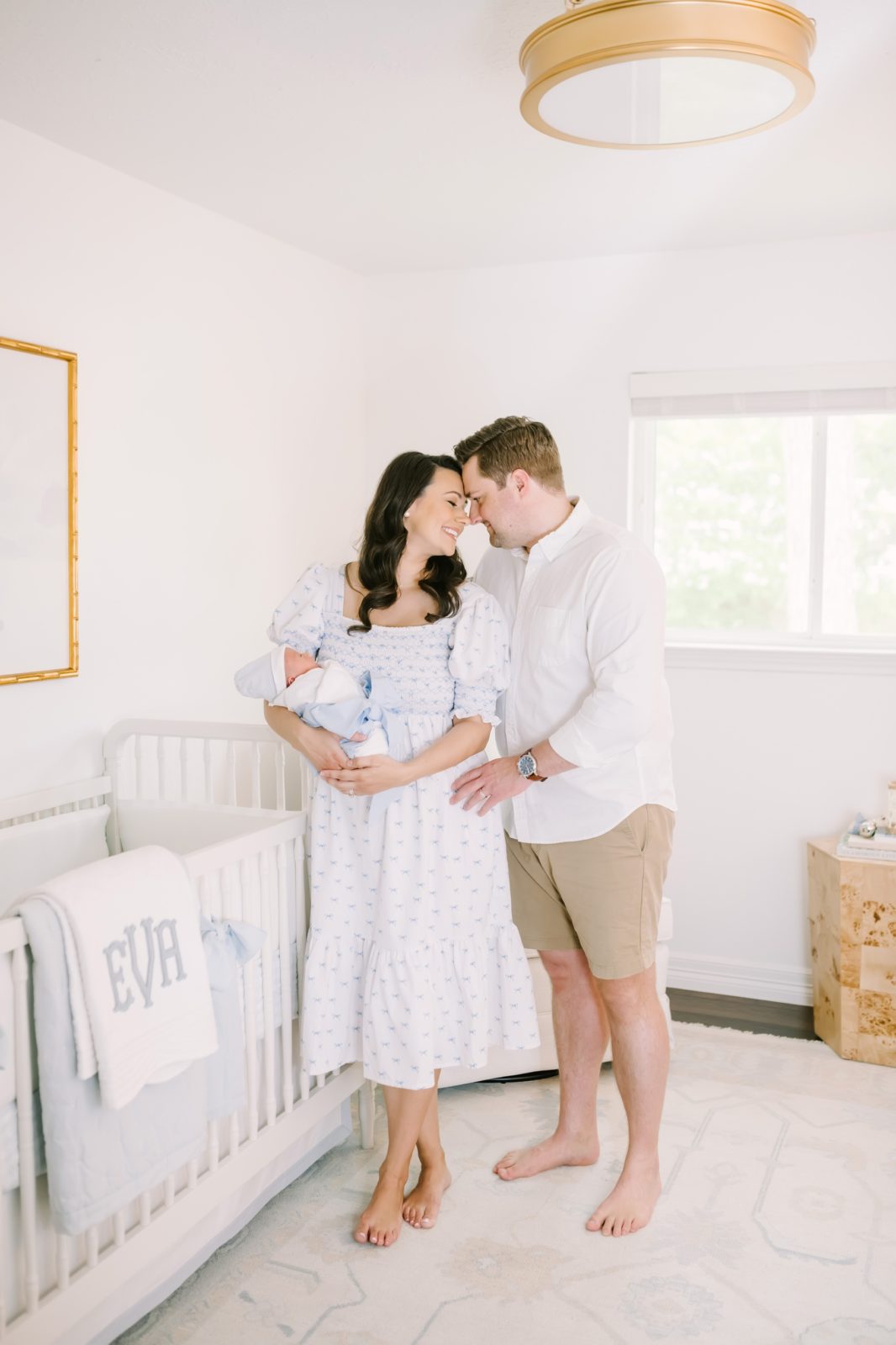 Standing in a neutral nursery a husband and wife cuddle together captured by Christina Elliott Photography. gold accents nursery Houston #ChristinaElliottPhotography #ChristinaElliottNewborns #HoustonLifestyleNewborns #HoustonFamilyPhotographer