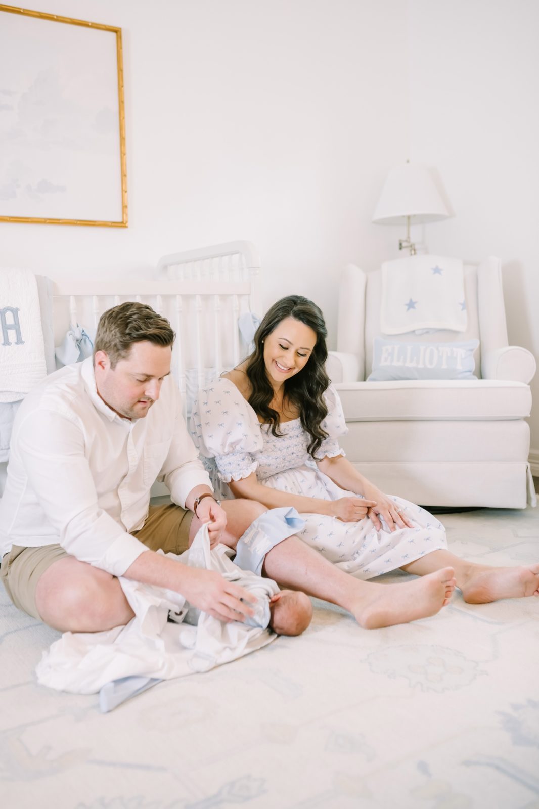 New parents smile down at their baby they are swaddling on the floor by Christina Elliott Photography. parents newborn baby lifestyle #ChristinaElliottPhotography #ChristinaElliottNewborns #HoustonLifestyleNewborns #HoustonFamilyPhotographer