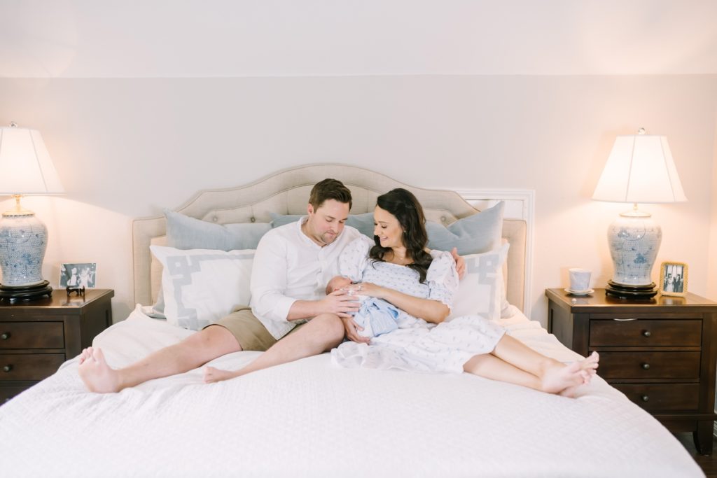 Sitting on a bed in a Houston home a mother and father look at their newborn by Christina Elliott Photography. newborn family portraits #ChristinaElliottPhotography #ChristinaElliottNewborns #HoustonLifestyleNewborns #HoustonFamilyPhotographer