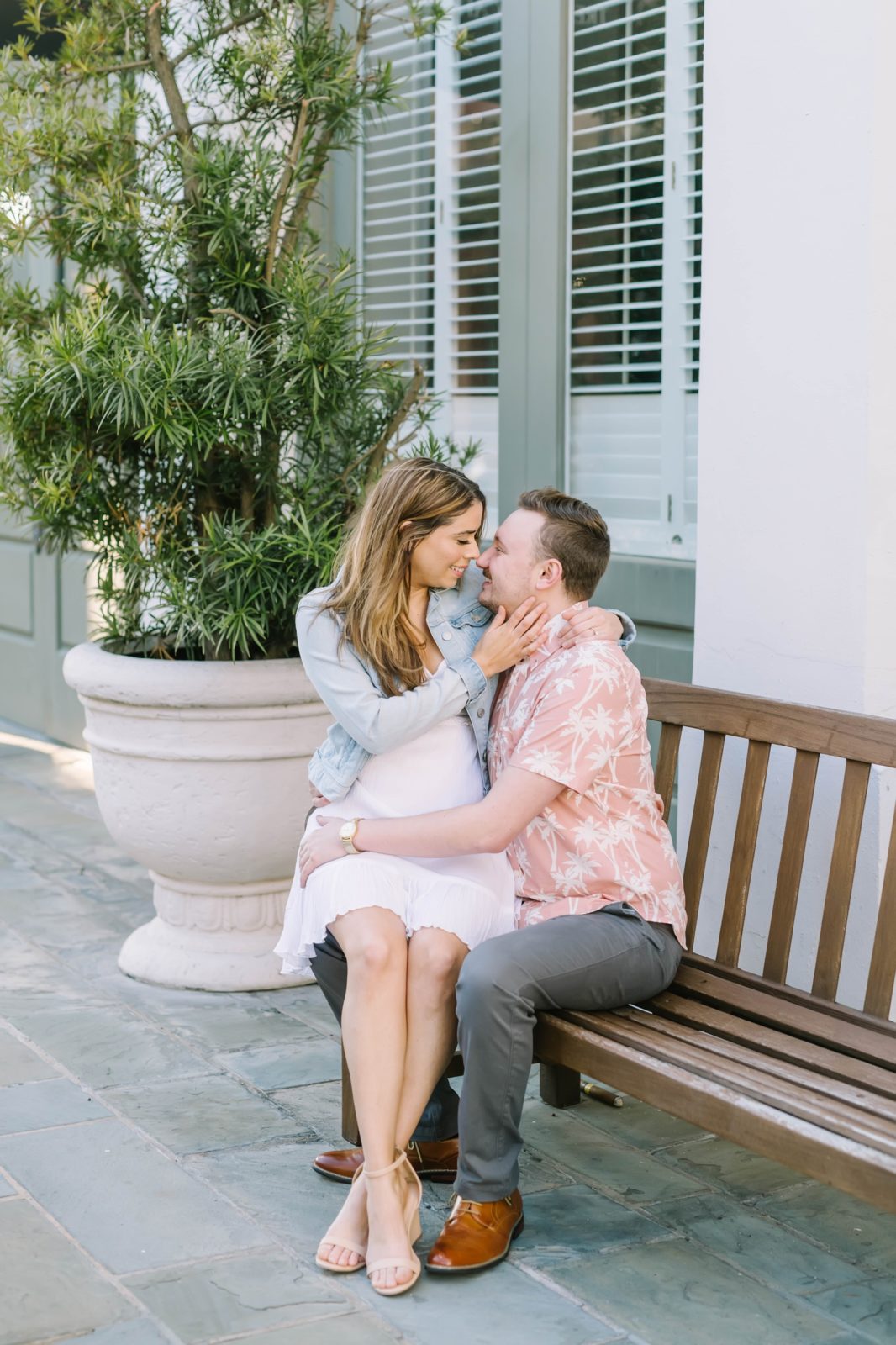 Woman sits on her fiances lap on a bench in Texas by Christina Elliott Photography. white dress and levi jacket button-up #ChristinaElliottPhotography #ChristinaElliottEngagements #TheTremontHouse #Texasengagements #shesaidyes