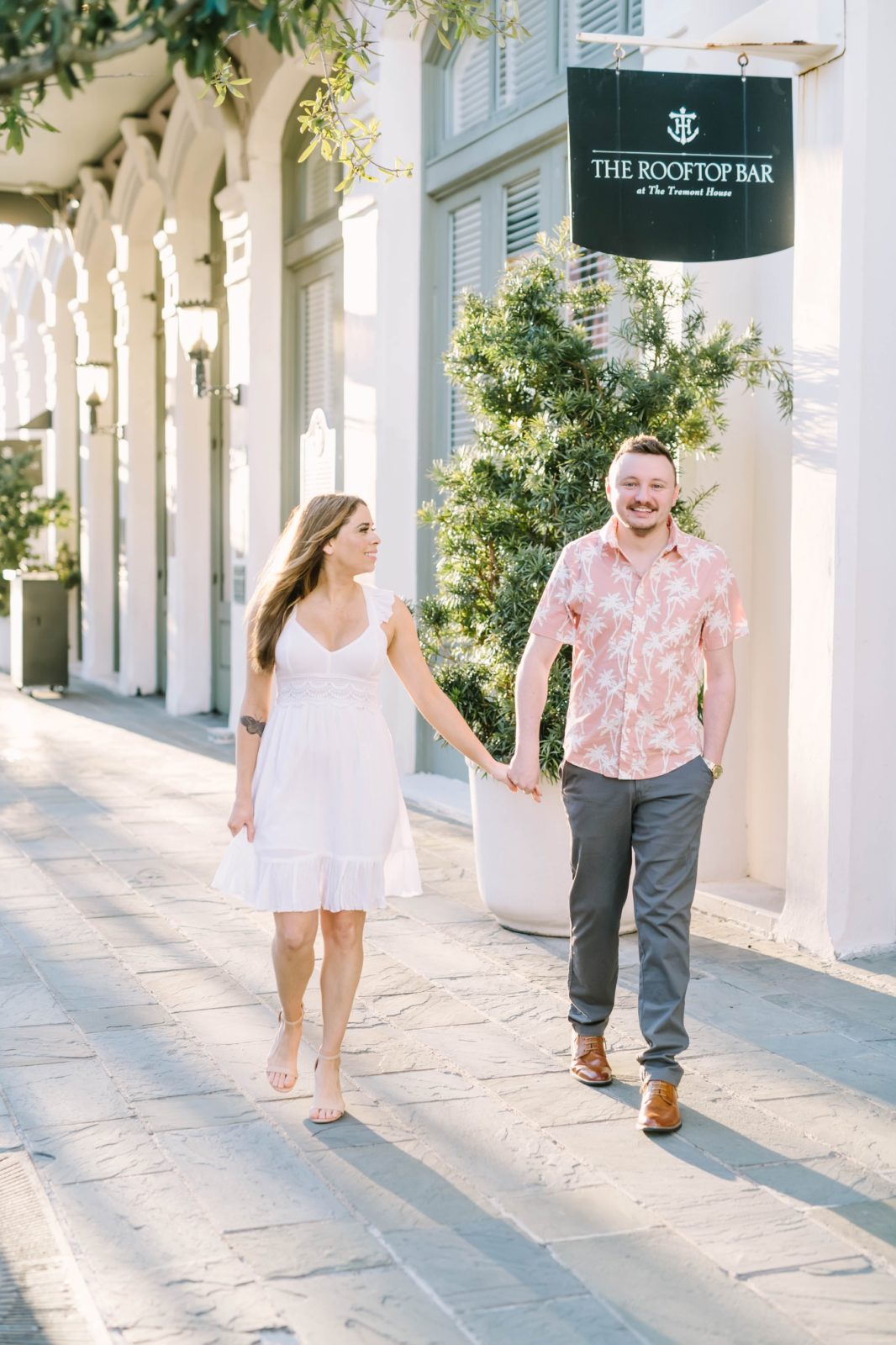 Holding hands walking down the street an engaged couple looks lovingly at one another by Christina Elliott Photography. summer Texas engagements #ChristinaElliottPhotography #ChristinaElliottEngagements #TheTremontHouse #Texasengagements #shesaidyes