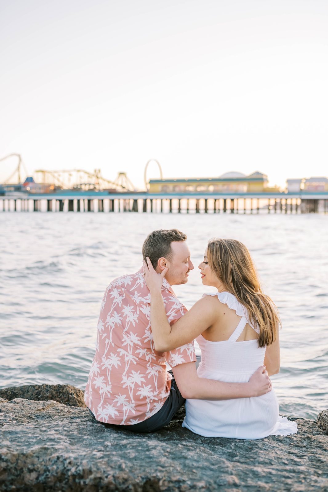 With an oceanside rollercoaster in the background an engaged couple kisses by Christina Elliott Photography. pier rollercoaster in love #ChristinaElliottPhotography #ChristinaElliottEngagements #TheTremontHouse #Texasengagements #shesaidyes