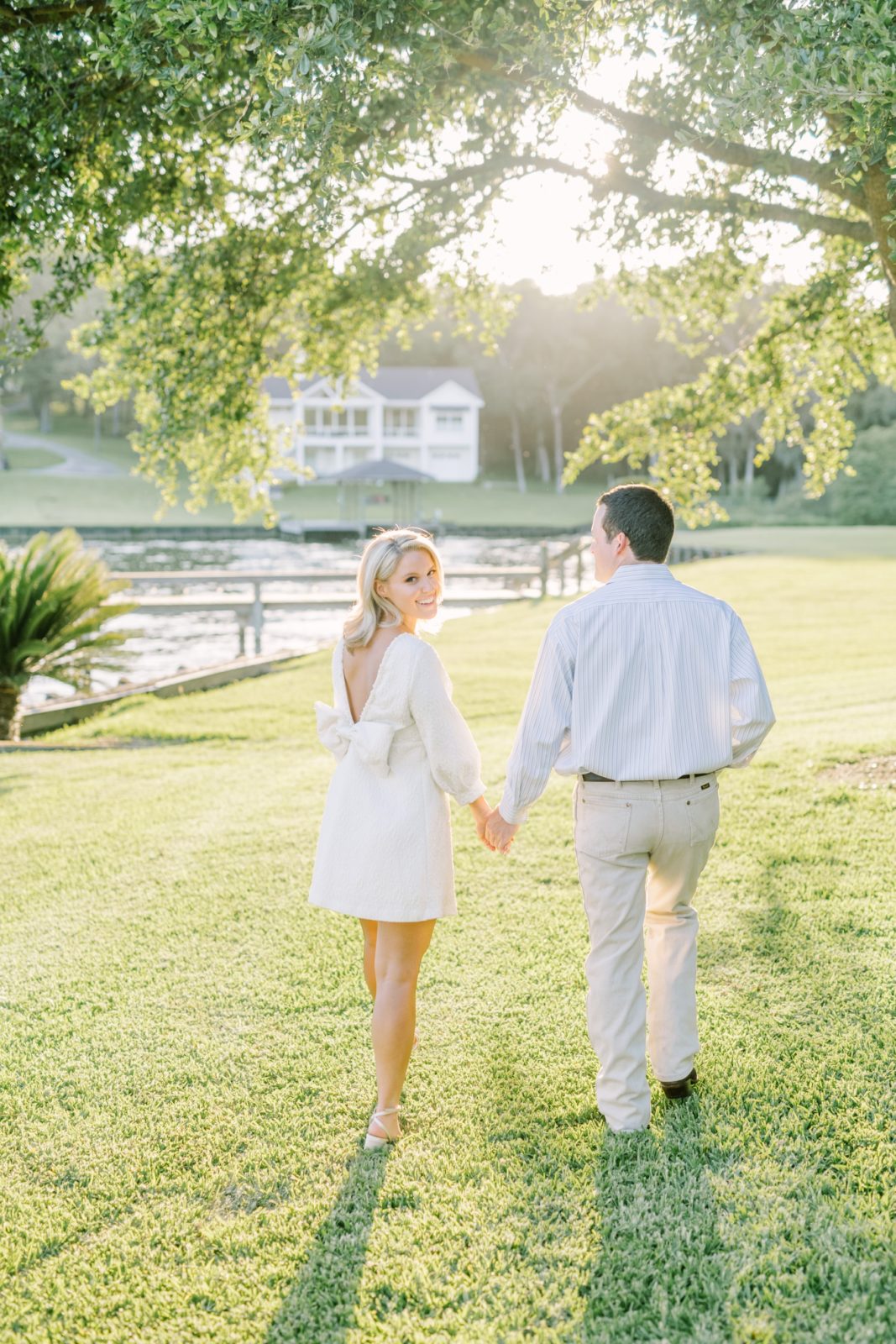 With the sun setting behind them, boyfriend and girlfriend walk hand in hand under a green tree by Christina Elliott Photography. romantic #ChristinaElliottPhotography #ChristinaElliottEngagements #LakeLivingston #summerengagements #Texasphotographer
