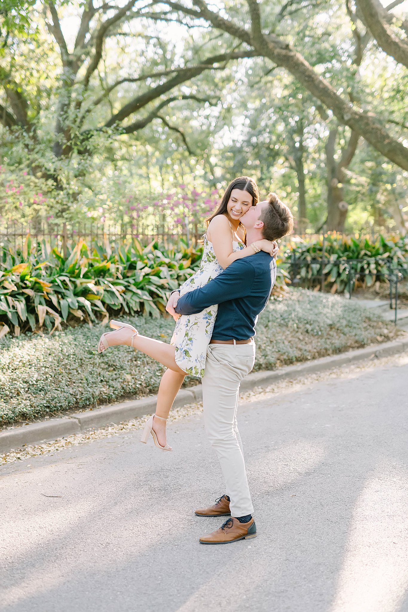 Man lifts bride to be and kisses her cheek during their Houston engagement session.